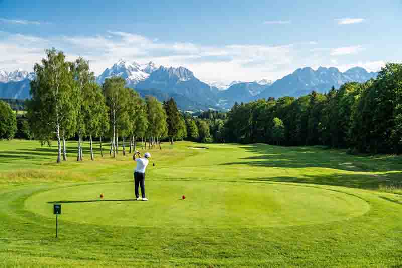 Golfspieler schlägt auf einem gepflegten Fairway in Oberbayern ab, im Hintergrund die schneebedeckten Gipfel der Bayerischen Alpen